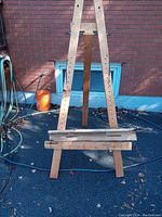 Front view of large wooden easel standing outdoors showing the three-legged frame and tray detached at bottom.