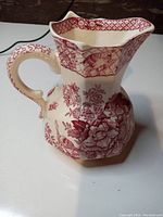 Front-side view of small red transferware ironstone water pitcher by Mason's, showing floral and geometric red patterns with ornate handle.