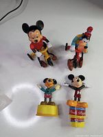 Four Disney character figurines: two 1977 Mickey and Goofy on tricycles, and two Mickey Mouse push puppets on bases.