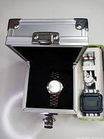 Photo showing the closed silver metal case with the analog casino promotional watch inside and the SpongeBob digital watch next to it.