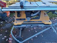 Side view of yellow Rigid collapsible table saw on metal stand with wheels, showing adjustable fence and power switch.