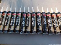 Thirteen tubes of Mulco Supra Expert white caulking laid out on a grey table in sunlight.