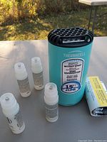 Front view of the Thermacell mosquito repellent device surrounded by four small repellent cartridges and a foil-wrapped fuel cartridge placed on a table outdoors.