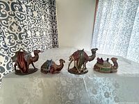Four ceramic nativity camels arranged on a table showing all figurines together
