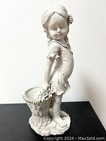 Front and side view of the white resin flower girl statue holding a basket with floral decorations, showing overall shape and detail.