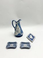 Photo showing tall Wedgwood jasperware jug with white relief design and three small jasperware trays/tiles all in light blue and white.