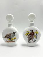 Two vintage milk glass decanters side by side showing both quail illustrations.