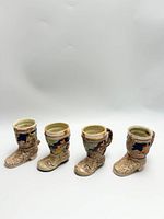 Front view of four decorative ceramic boots with detailed hand-painted scenes and embossed floral texture.