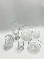 Full view of 6 glass baskets arranged against white background showing varied shapes and handle styles, highlighting overall condition and design.