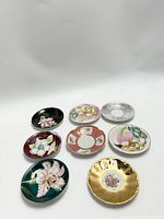 Seven vintage ceramic plates with various hand-painted floral designs photographed from above on white background.