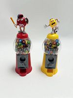 Lot of two M&M candy dispensers, one red with baseball character and one yellow with soccer character, filled with colorful M&M candies.
