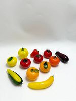 Group of 11 Murano style glass fruit figurines shaped as tomatoes, bell pepper, orange, banana, corn, and eggplant on a white background.