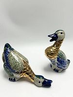 Front view of two vintage duck figurines, one upright and one pecking, showcasing blue, green, white ceramic with brass accents.