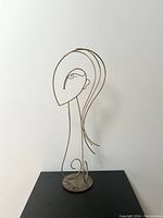 Full view of the brass and steel wire female sculpture on black surface with simple round base.