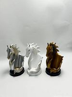 Front view of 3 resin horse head wine bottle bottom holders in silver, white and bronze.
