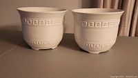 Two large white ceramic flower planters side by side on a table, showing full size and shape.