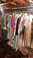 Photo of three clothing racks filled with assorted vintage women's clothing items including dresses, blouses, skirts, and jackets in various muted and pastel colors.