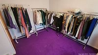 Four racks filled with assorted vintage clothing items including tops, pants, and dresses in various colors and patterns hung on plastic and metal hangers.