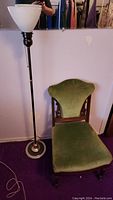 Photo of floor lamp next to antique parlour chair with green velvet upholstery