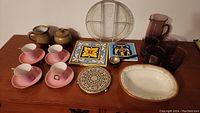 Wide view of all collectible items on table including cups, saucers, pots, plates, glassware and coaster