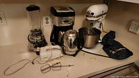 Wide view of all items in the lot on counter: KitchenAid stand mixer with bowl, Osterizer blender, coffee maker, handheld mixer and beaters.