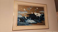 Framed print showing two white Asian cranes in a stylized natural scene with foliage and water, in a light wood or faux wood frame with cream matting.