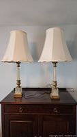 Pair of tall Mid-Century Modern Hollywood Regency style table lamps on wooden cabinet, wired with beige fabric lampshades