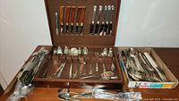 Overview of the boxed silverplate cutlery lot including knives, forks, spoons, serving utensils, and salt and pepper shakers spread across a case and tray.