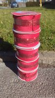 Stack of five rolls of red velvet Christmas ribbon with a red sparkle accent on white spool cores.