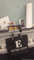 Elton John black tote bag and contents including booklet, VIP pass keychain, and rolled posters.