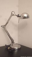 Side view of the fully articulating industrial style desk lamp on a black surface, lamp extended vertically.