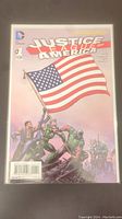Front cover of Justice League of America #1 comic book showing heroes raising American flag.