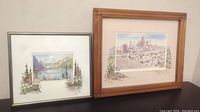 Two framed Marilyn Kinsella watercolor prints, one of Lake Louise and one of Calgary Skyline, shown side by side.