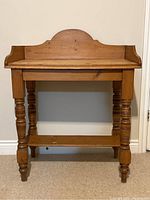 Front view of antique pine washstand showing scalloped splash back, turned legs, and lower stretcher shelf.