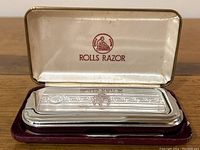 Top view of closed razor kit case with Rolls Razor logo inside lid and silver-tone metal razor visible on velvet lining.