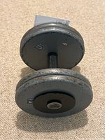 Metal dumbbell on carpet with weight plates marked '10' visible and measuring tape beside it to show size.