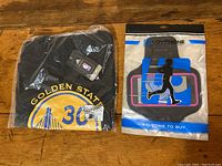 Photo of Golden State Warriors Stephen Curry jersey in plastic packaging alongside blue and black running armband also in retail package.
