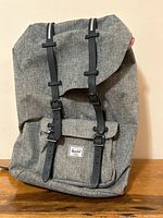 Grey Herschel backpack front view showing magnetic leather straps, front pocket with Herschel label, and fabric texture