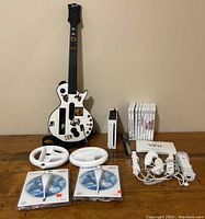 Full lot showing Nintendo Wii console, nine game cases, three remotes, dance pad, two steering wheels, and guitar hero controller guitar