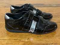 Side view of the pair of black Prada sneakers showing the patent leather finish and silver accent on the Velcro straps.