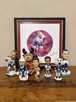 Front view of lot showing all bobbleheads, Calgary Flames plush deer, and framed signed Mike Bossy painting in background.