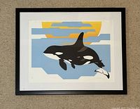 Framed print depicting a stylized orca whale with a rising sun, geometric shapes for water and sky, colors include black, white, yellow-orange, blue, and gray