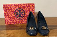 Front view of Tory Burch wedge shoes in dark blue leather with the original box behind