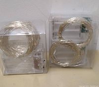Photo showing two packs of coiled wire fairy lights with small LED bulbs in clear plastic packaging.