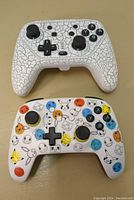 Photo of the front side of two Nintendo Switch controllers, one white with cracked pattern and one white with colorful Pokémon-themed icons.