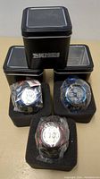Three Skmei digital sport watches in black foam holders, wrapped in plastic, in front of three black Skmei branded metal tins with transparent lids.