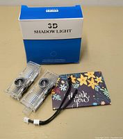 Photo of the two clear LED light parts, wiring with connectors, blue and white product box labeled '3D Shadow Light', and floral thank you card.