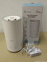 Front view of Acare Top Fill Aroma Humidifier next to its product box and power adapter with USB cable.