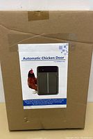 Box packaging showing the label 'Automatic Chicken Door' with an image of the door and a chicken, indicating the product purpose and branding.