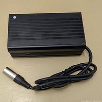 Top view of black rectangular battery charger with ribbed design and attached cable with metal connector.